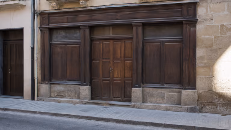 Fachada neutra de piedra y madera, puerta cerrada, sin texto, sin personas y sin productos.